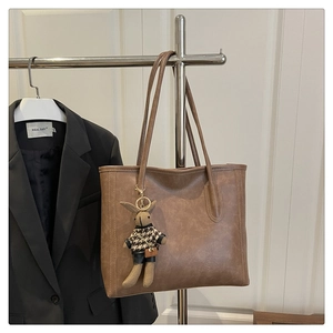 Detail of a brown faux leather tote bag featuring a cute houndstooth bunny doll charm