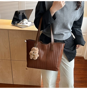 Brown woven leather tote bag with long straps and a plush puppy pendant in use