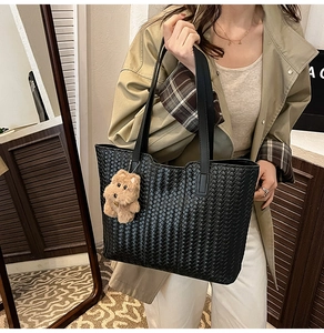 Detailed view of the black woven tote bag texture featuring a cute plush bear pendant