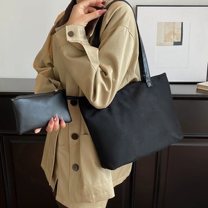 Minimalist black PU leather tote bag with matching pouch set worn by a model in a modern room