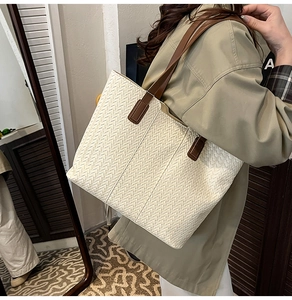 Detail of model wearing a large cream woven tote bag with brown leather shoulder straps