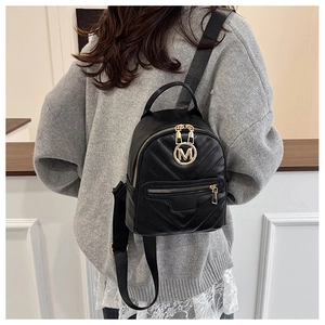 Detail of black quilted mini backpack featuring gold M logo and adjustable nylon straps