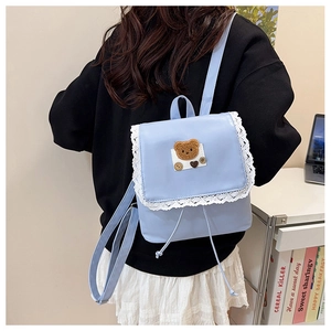 Détail du sac à dos bleu clair avec bordure en dentelle blanche et patch ours en peluche