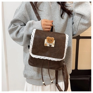 Détail d'un mini sac à dos en cuir marron vintage avec bordure dentelle et broderie ours