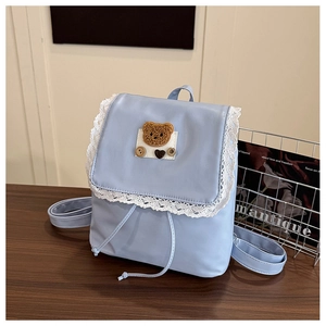Détail d'un mini sac à dos bleu clair avec bordure en dentelle et écusson ours en peluche
