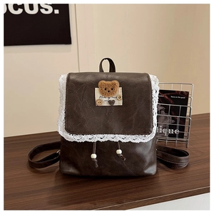 Détail d'un sac à dos vintage marron avec bordure en dentelle et patch d'ours en peluche