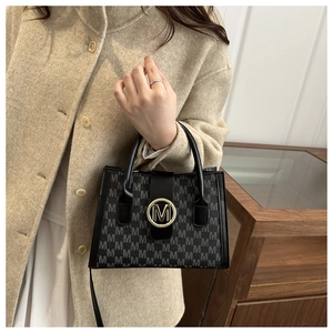 Detail of black crossbody bag featuring M-pattern print and gold metallic buckle