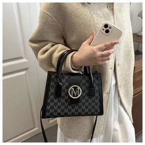 Macro view of leather crossbody bag featuring gold M-buckle and monogram pattern