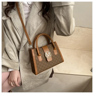 Detail of a brown crossbody bag featuring golden M logo and monogram canvas pattern