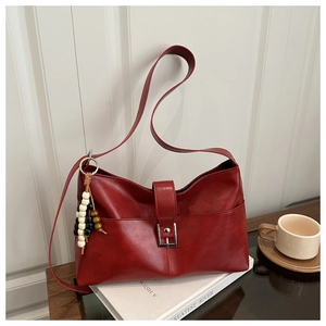 Close-up of retro red leather shoulder bag with silver buckle and beaded pendant on books