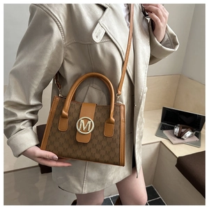 Detail of the brown monogram crossbody bag with a gold metal M logo and leather strap