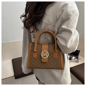 Brown monogram crossbody bag with metallic M-logo buckle worn by model on a bench