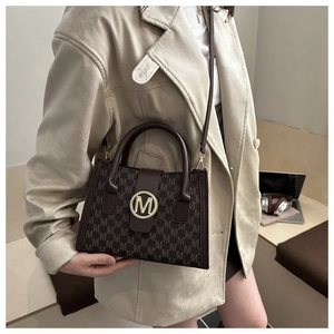 Detail view of brown crossbody bag with all-over M pattern and gold metal buckle