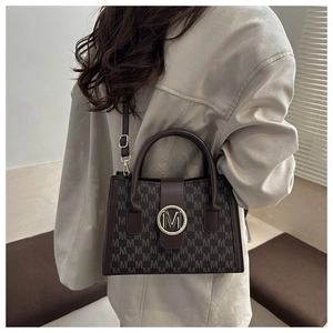 Detail of dark brown crossbody bag with letter M print and gold metal logo on blazer