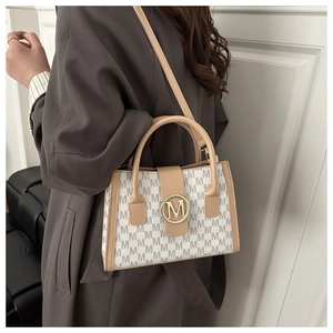 Detail view of stylish beige crossbody bag with M-pattern and gold logo emblem
