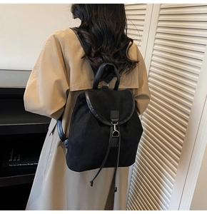 Détail d'un sac à dos en daim noir avec rabat supérieur, liseré en cuir et cordon de serrage