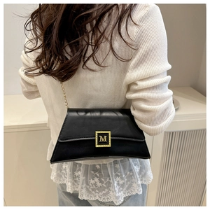 Detail view of a black leather shoulder bag featuring a square gold M-shaped metal clasp