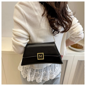 Detail of black faux leather shoulder bag featuring a gold M letter metal buckle