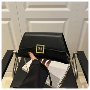 Detail of black leather crossbody bag featuring gold chain and embossed M logo buckle