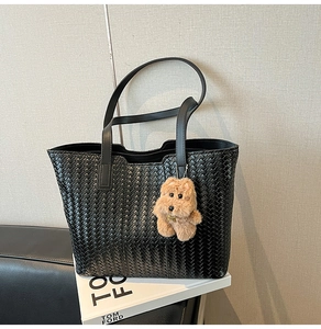 Detail of black woven leather tote bag with a cute brown plush puppy charm