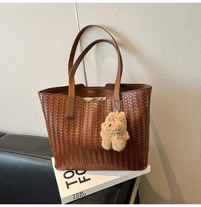 Macro view of woven dark brown leather tote bag with small plush dog charm detail