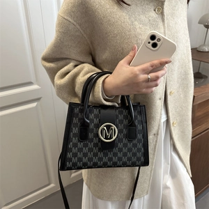 Chic crossbody bag with 'M' letter print and gold buckle on a stylish model