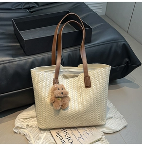 Detail of beige woven tote bag with brown handles and cute plush dog charm accessory