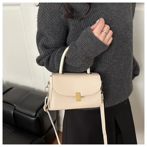 Detail of cream white crossbody bag with matte gold buckle held by a model