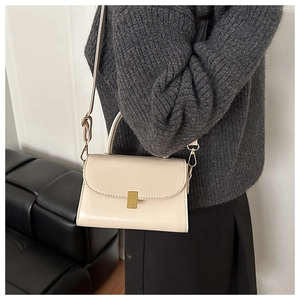 Detail of off-white crossbody bag with golden clasp worn over a grey knit sweater