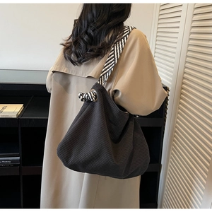 Detail view of black corduroy hobo bag with striped strap and decorative knot detail