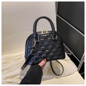 Detailed close-up of a black checkered shell bag with golden zippers and leather straps