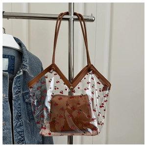 Detail view of transparent PVC tote bag featuring cherry print and brown leather handles