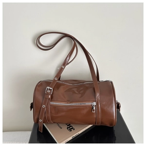 Detailed view of dark brown cylindrical shoulder bag with silver zipper and studded strap