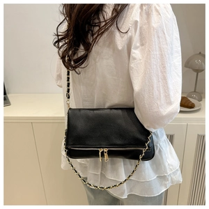 Detailed close-up of a black litchi pattern leather bag with gold chain strap on model