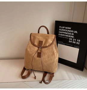 Close-up of brown suede backpack with leather trim and metal hook closure on marble table