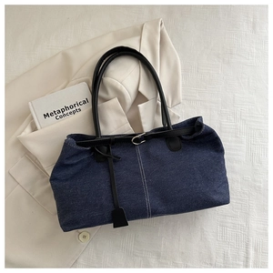 Detailed top view of a dark blue denim tote bag with white stitching on a beige blazer