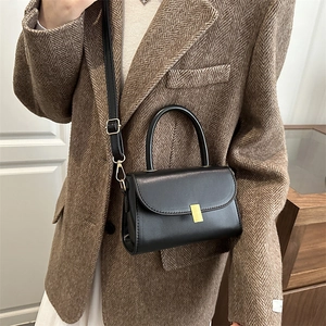 Minimalist black faux leather handbag with gold metal clasp on a textured blazer