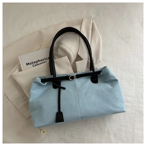 Detail of light blue denim tote bag with black leather straps and metal buckle accents