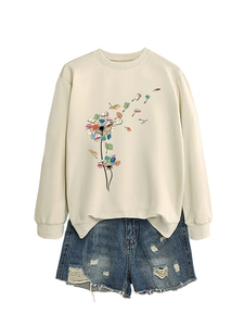 Detail showing dandelion book graphic on a cream long sleeve sweatshirt with frayed denim shorts