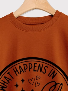 Detail of burnt orange sweatshirt showing ribbed crew neck and What Happens In print