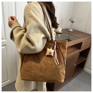 Detailed close-up of brown suede tote bag with cartoon print and plush bread charm
