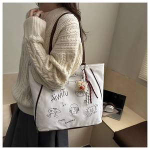Detail of white canvas tote bag with brown leather straps and cute cartoon illustrations