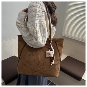 Braune Wildleder-Tote Bag mit Graffiti und Plüsch-Anhänger an der Schulter des Models