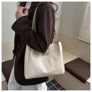 Détail du sac cabas crème avec bandoulière chaîne en cuir vert et étiquette tendance
