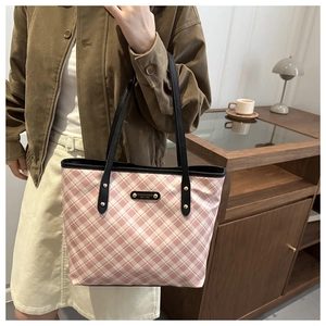 Close-up of pink checkered tote bag with black leather handle and metal logo plate