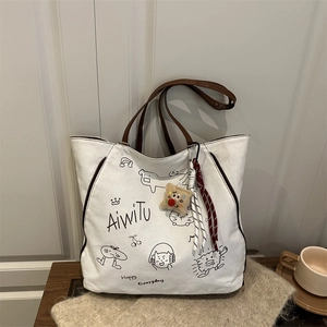 White canvas tote bag with cartoon cat print and brown handles on a soft beige blanket