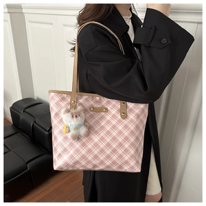 Detail of pink plaid tote bag with leather handles and cute bear charm on black coat