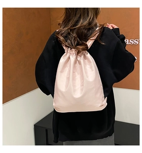 Rear view of a light pink drawstring backpack in glossy satin fabric worn by a model