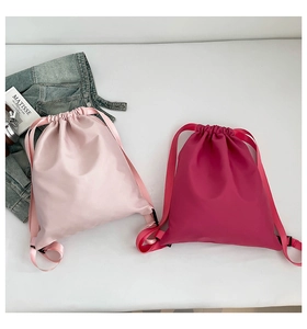 Flat lay of light pink and magenta nylon drawstring bags with a casual denim jacket