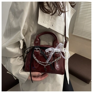 Dettaglio mini borsa bordeaux con catene metalliche, ciondolo a croce e fiocco in pizzo bianco